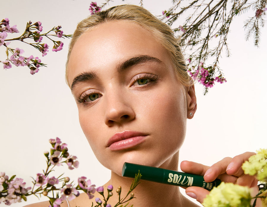 The Root 1 lash serum applicator held up among blossom branches